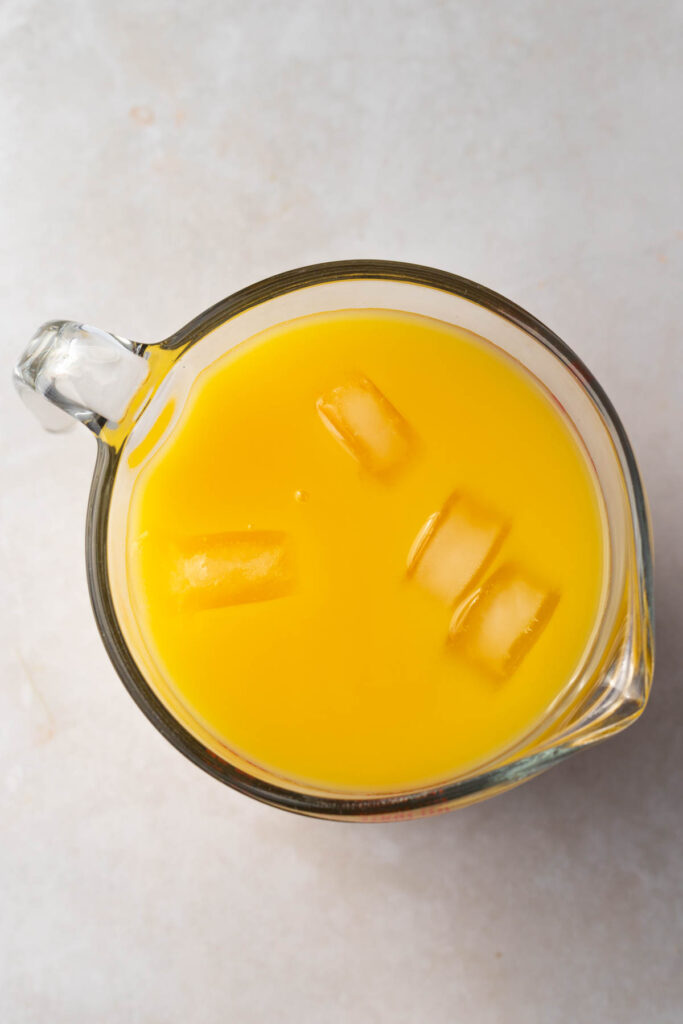 large measuring cup of cold orange juice with 4 ice cubes