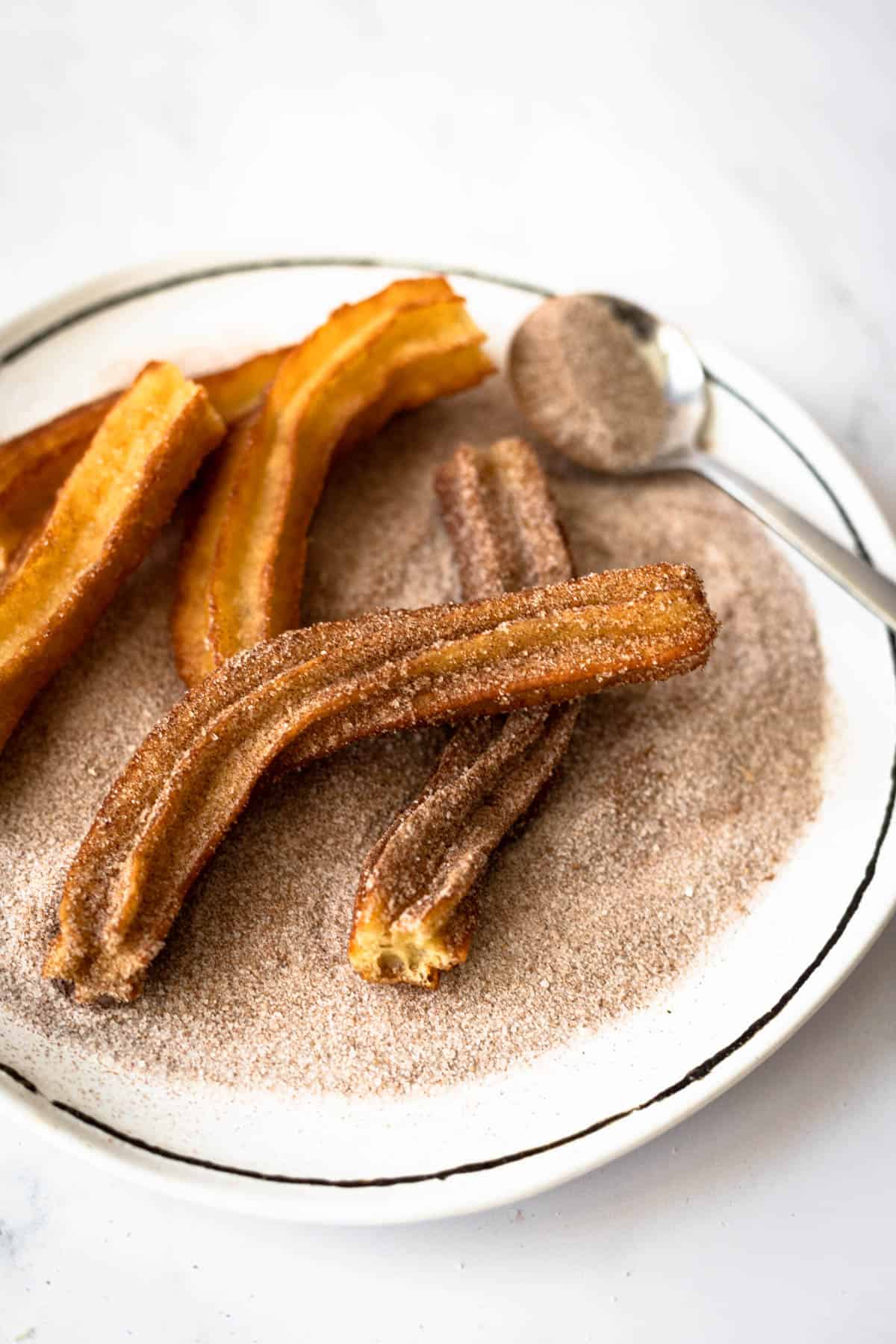 dusted churros on a plate of cinnamon/sugar