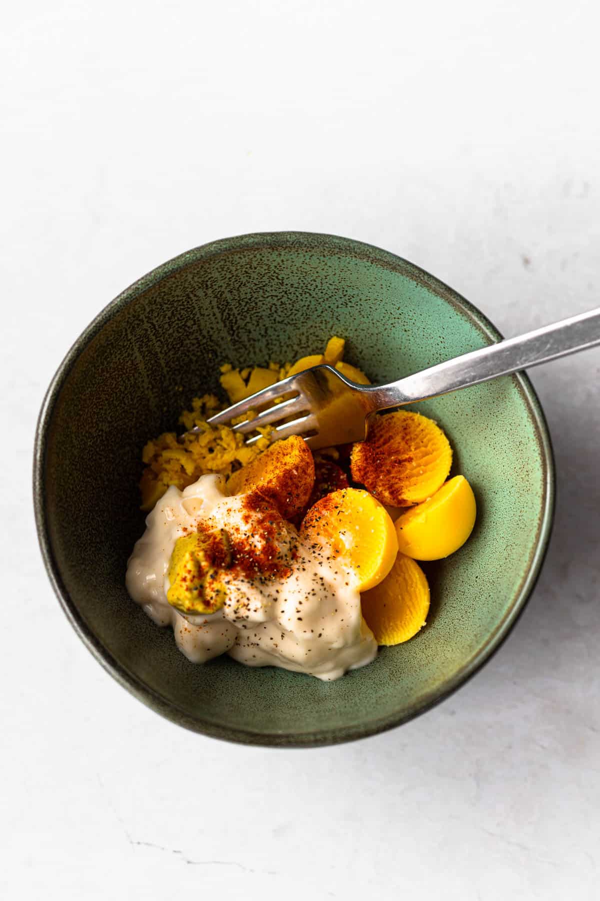 process shot showing egg yolks, miracle whip, paprika, dijon mustard being combined in a bowl