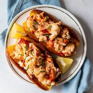 two connecticut style lobster rolls on a plate garnished with lemon wedges