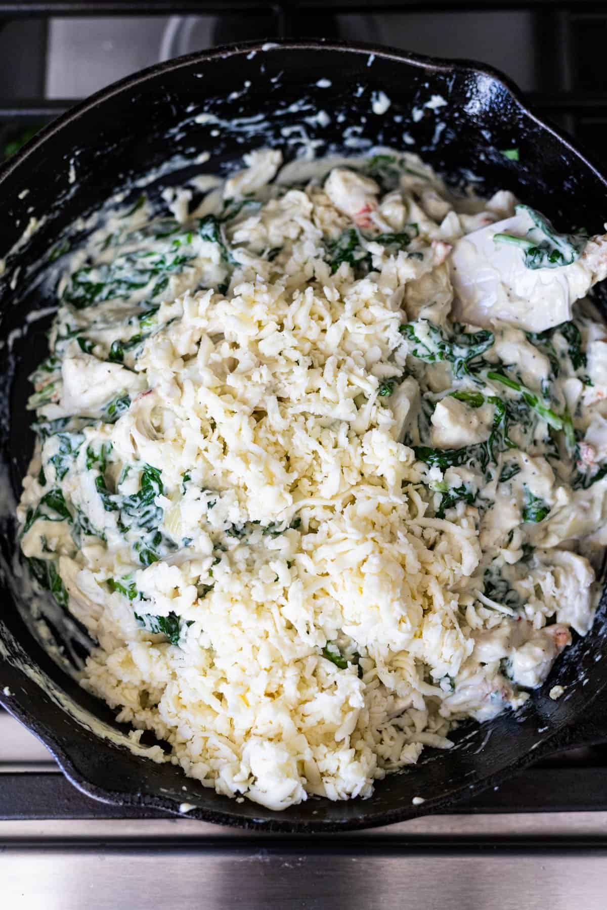 shredded mozzarella cheese added to the skillet of spinach and crab dip
