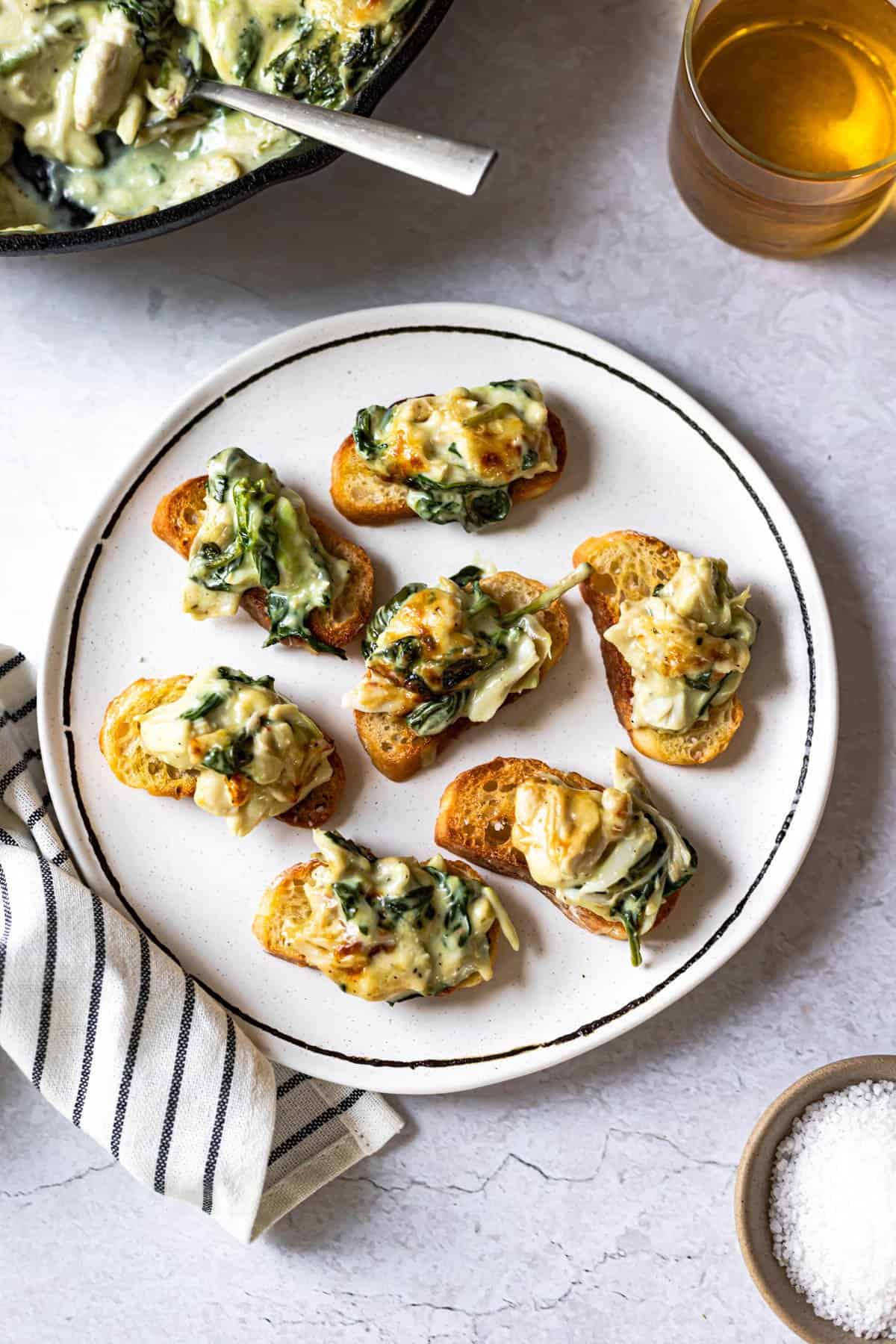 spinach crab and artichoke dip served on pieces of crostini on a white plate
