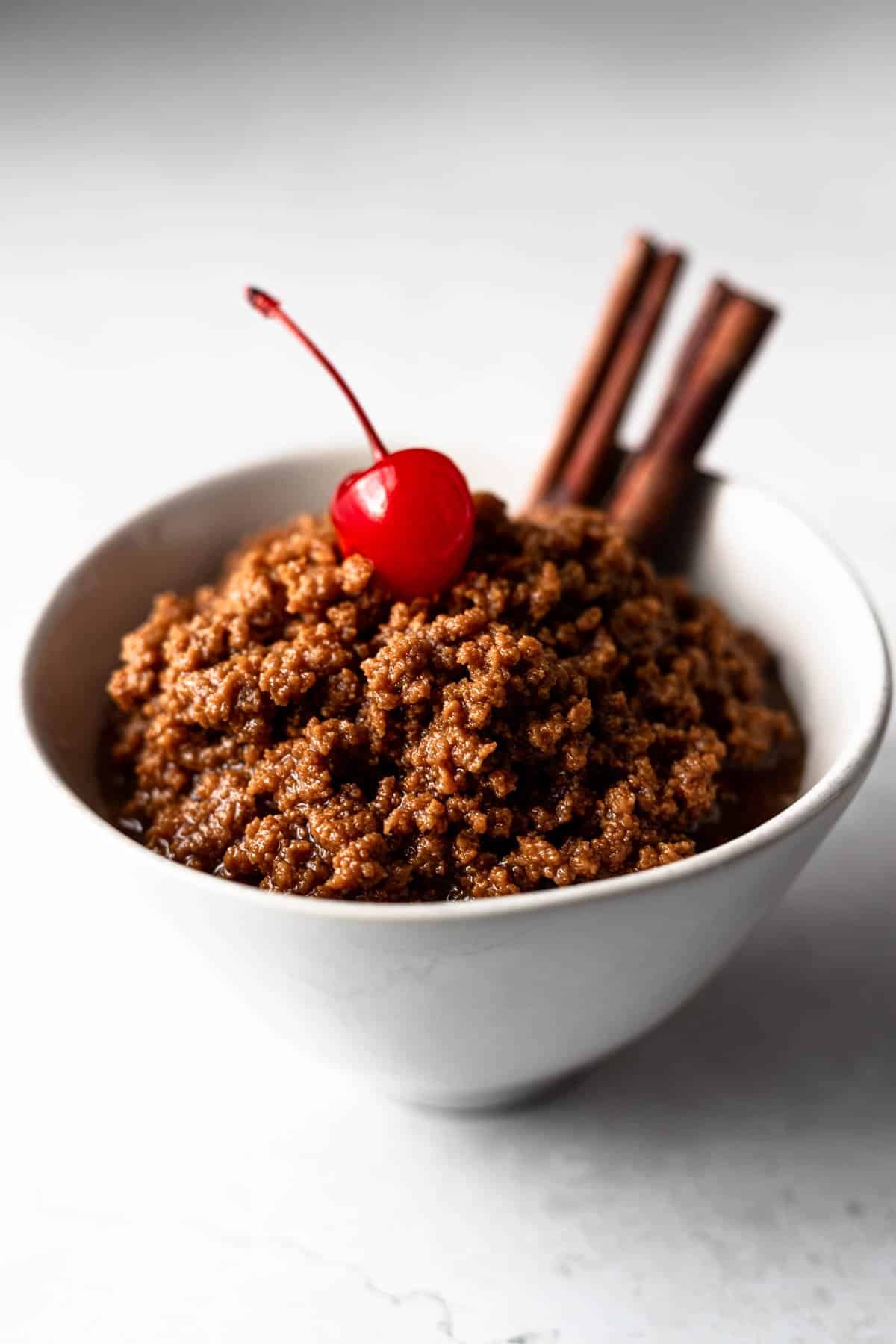small bowl of dulce de leche cortada topped with a cherry and garnished with cinnamon sticks