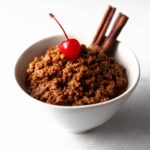 small bowl of dulce de leche cortada topped with a cherry and garnished with cinnamon sticks
