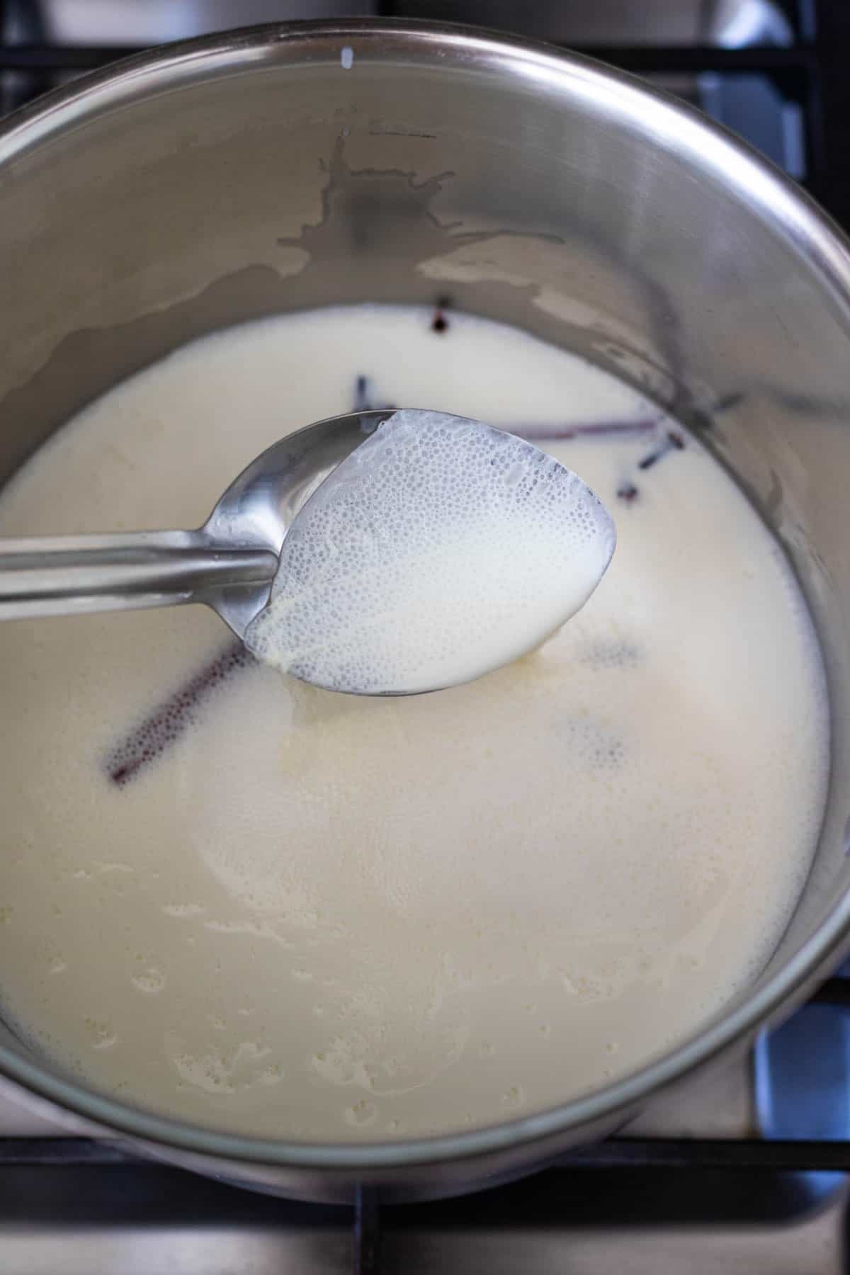 warm milk with a layer of film shown on a spoon