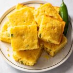 jalapeño cornbread cut into squares on a white plate.