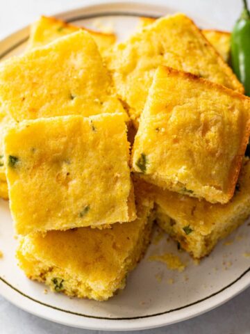 jalapeño cornbread cut into squares on a white plate.