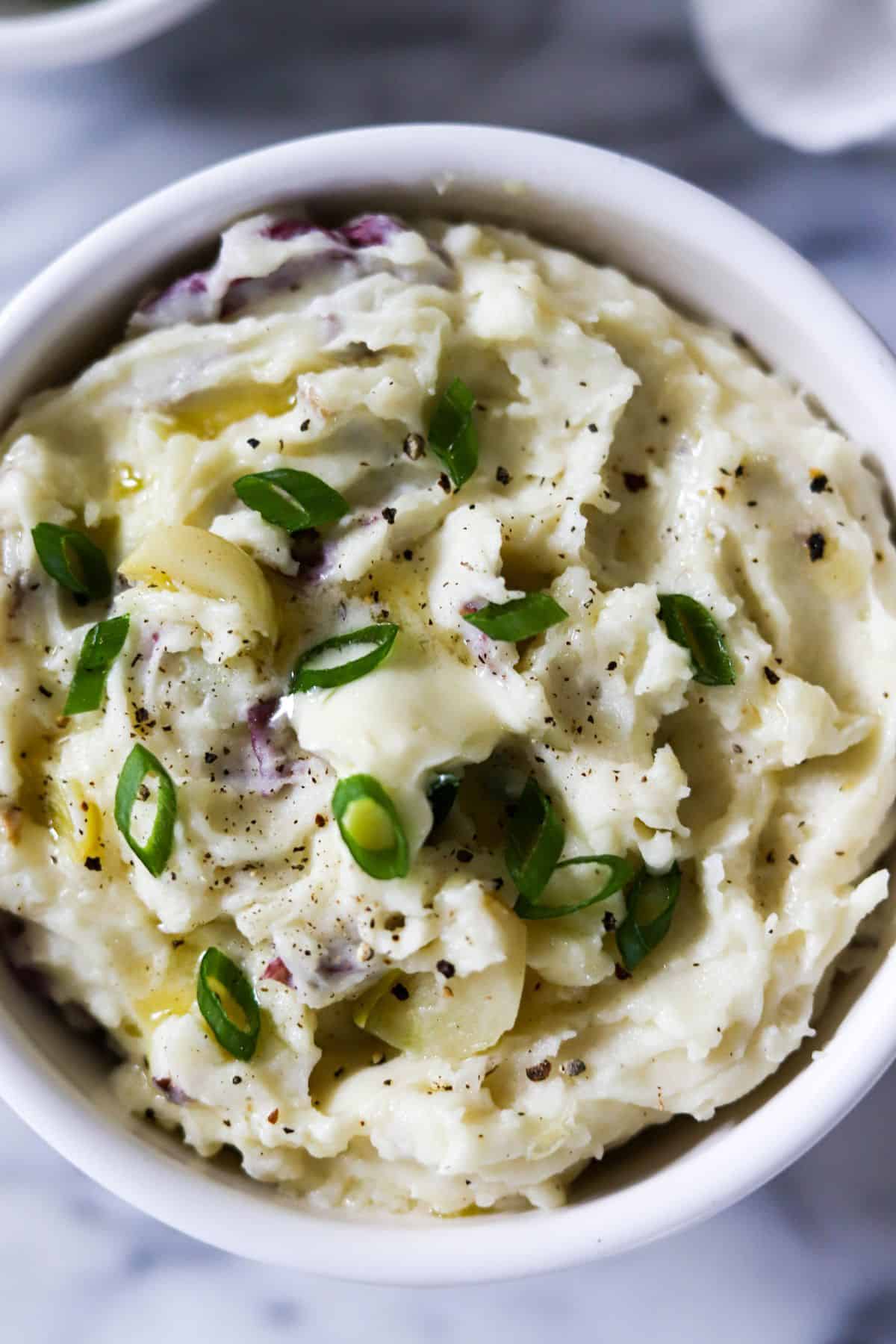 bowl of mashed potatoes with red skin topped with butter, black pepper and sliced green onions.