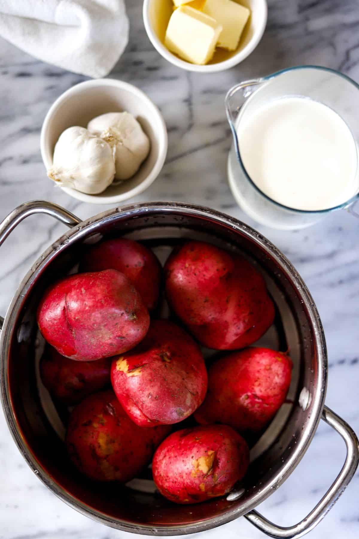 ingredients for mashed potatoes with red skin - cubes of butter, 2 heads of garlic, heavy cream and red skinned potatoes.