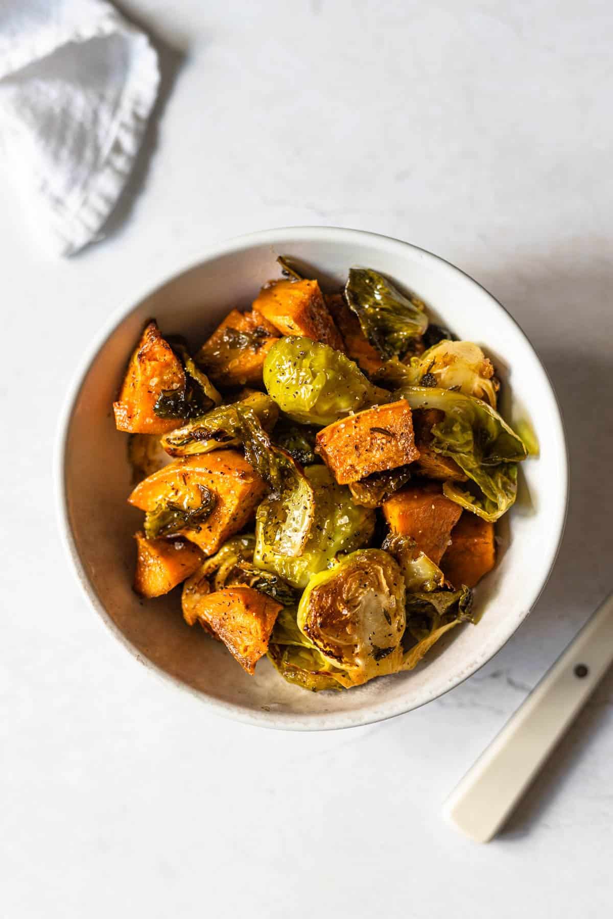 roasted brussels sprouts and sweet potato chunks in a white bowl.