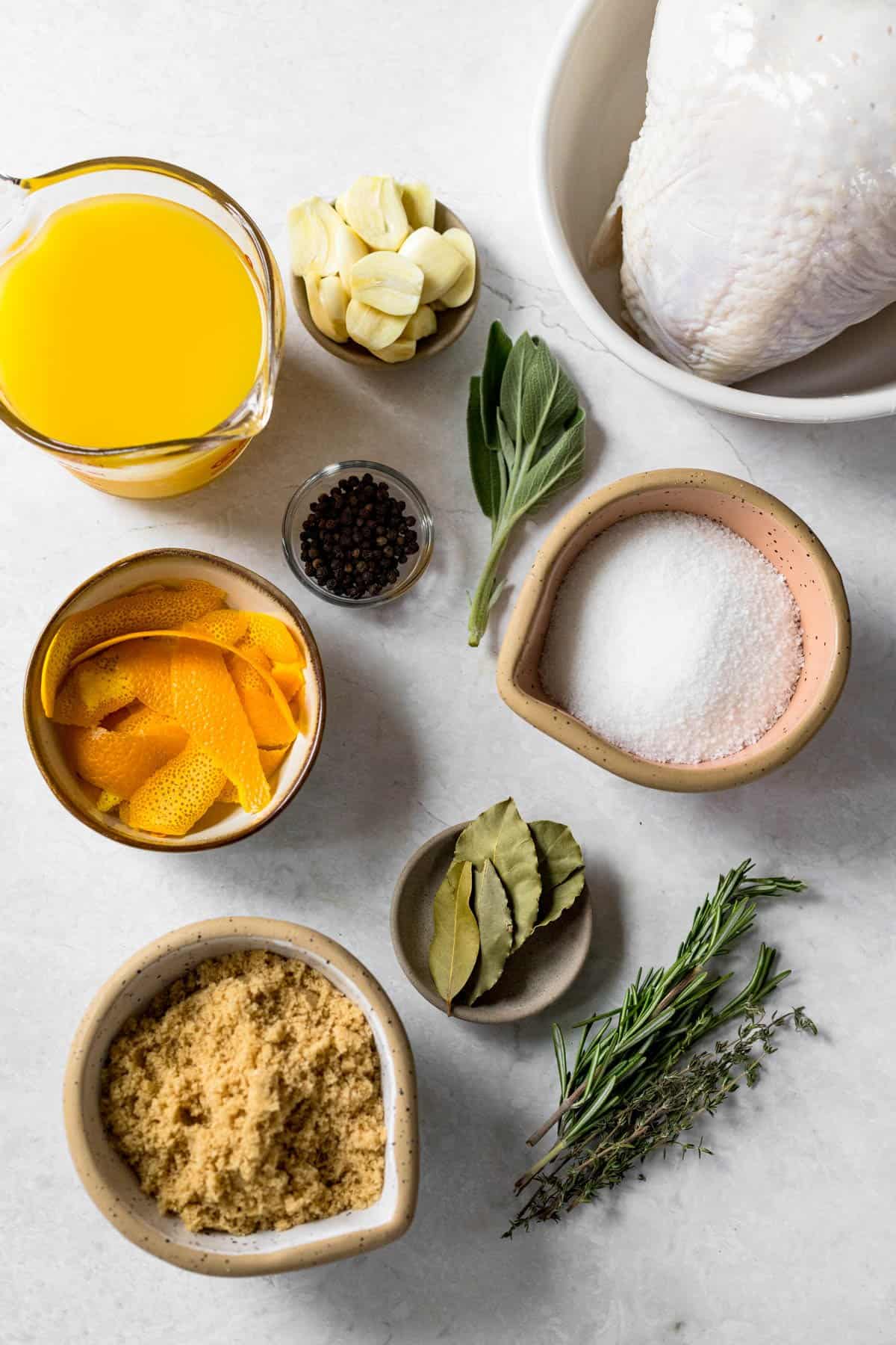 brine ingredients - orange juice, garlic cloves, sage leaves, turkey breast, salt, black peppercorns, orange peels, bay leaves, brown sugar, rosemary, thyme.