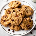 chocolate chip pecan cookies on white plate with chocolate chips scattered in background.