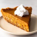 slice of pumpkin pie on a graham cracker crust topped with whipped topping.