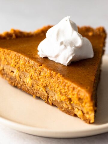 slice of pumpkin pie on a graham cracker crust topped with whipped topping.