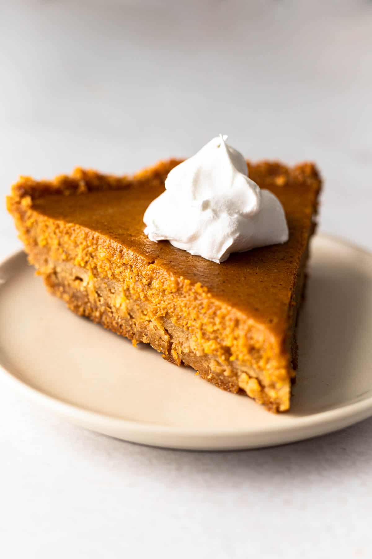 slice of pumpkin pie on a graham cracker crust topped with whipped topping.