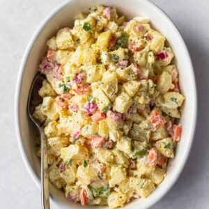 Olivier salad in a round white dish shown with a serving spoon.