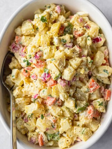 Olivier salad in a round white dish shown with a serving spoon.