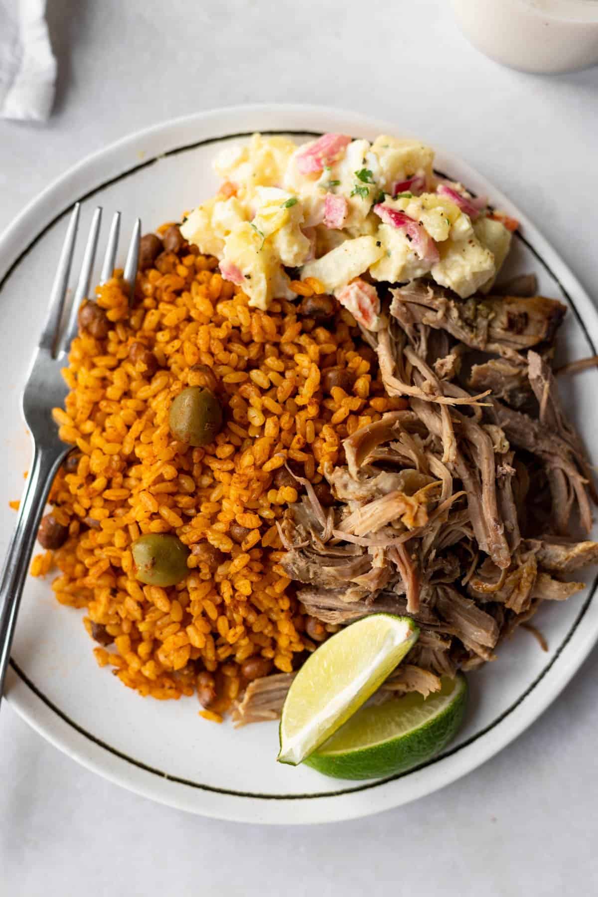 olivier salad served with shredded pork shoulder, rice and pigeon peas on a white plate with a black rim.