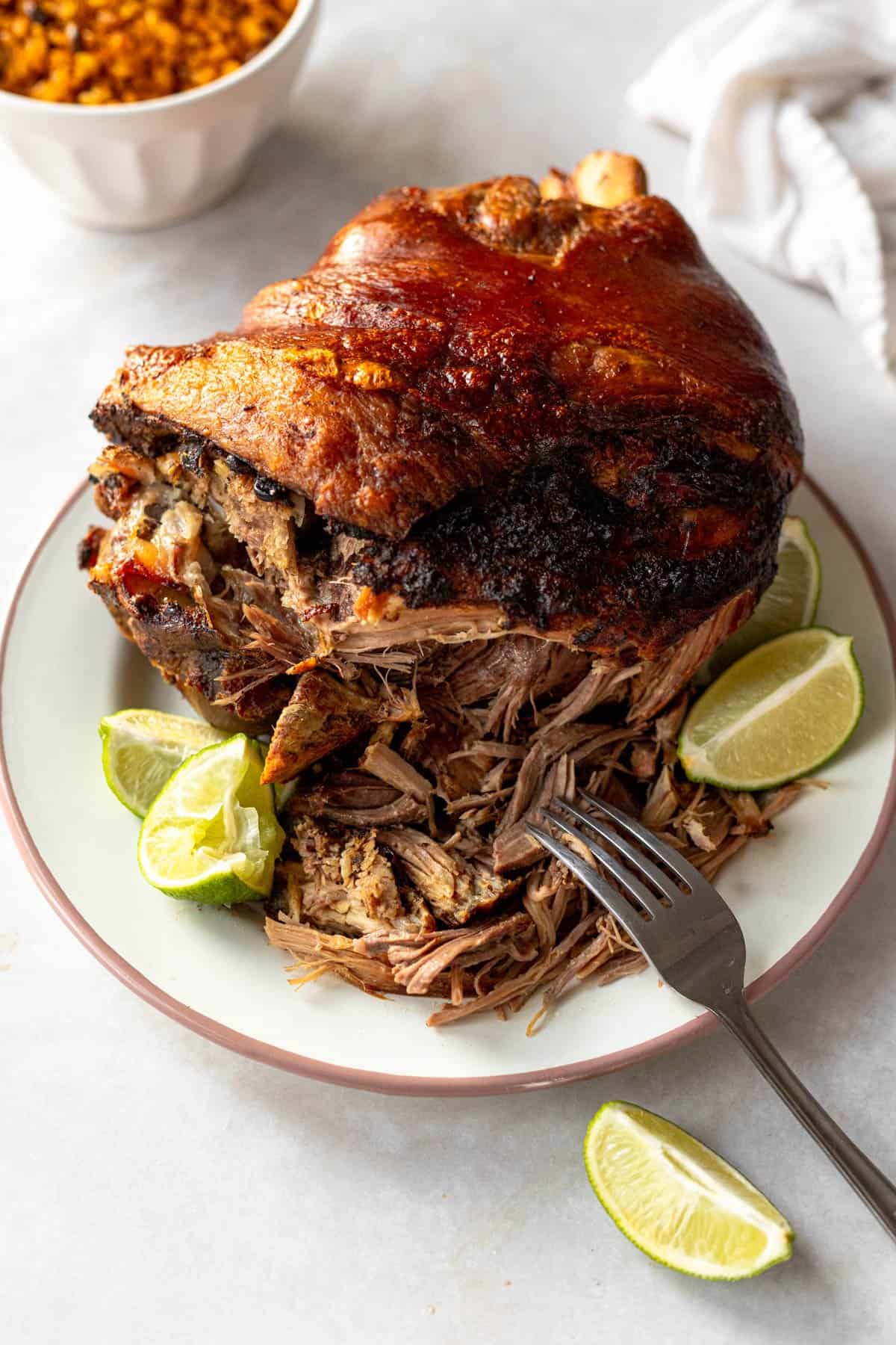 shredded roast pork shoulder (pernil) on a platter shown with limes and crispy skin.