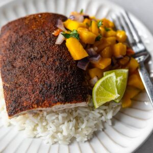 blackened mahi mahi on a bed of white rice served with mango salsa on a white plate.