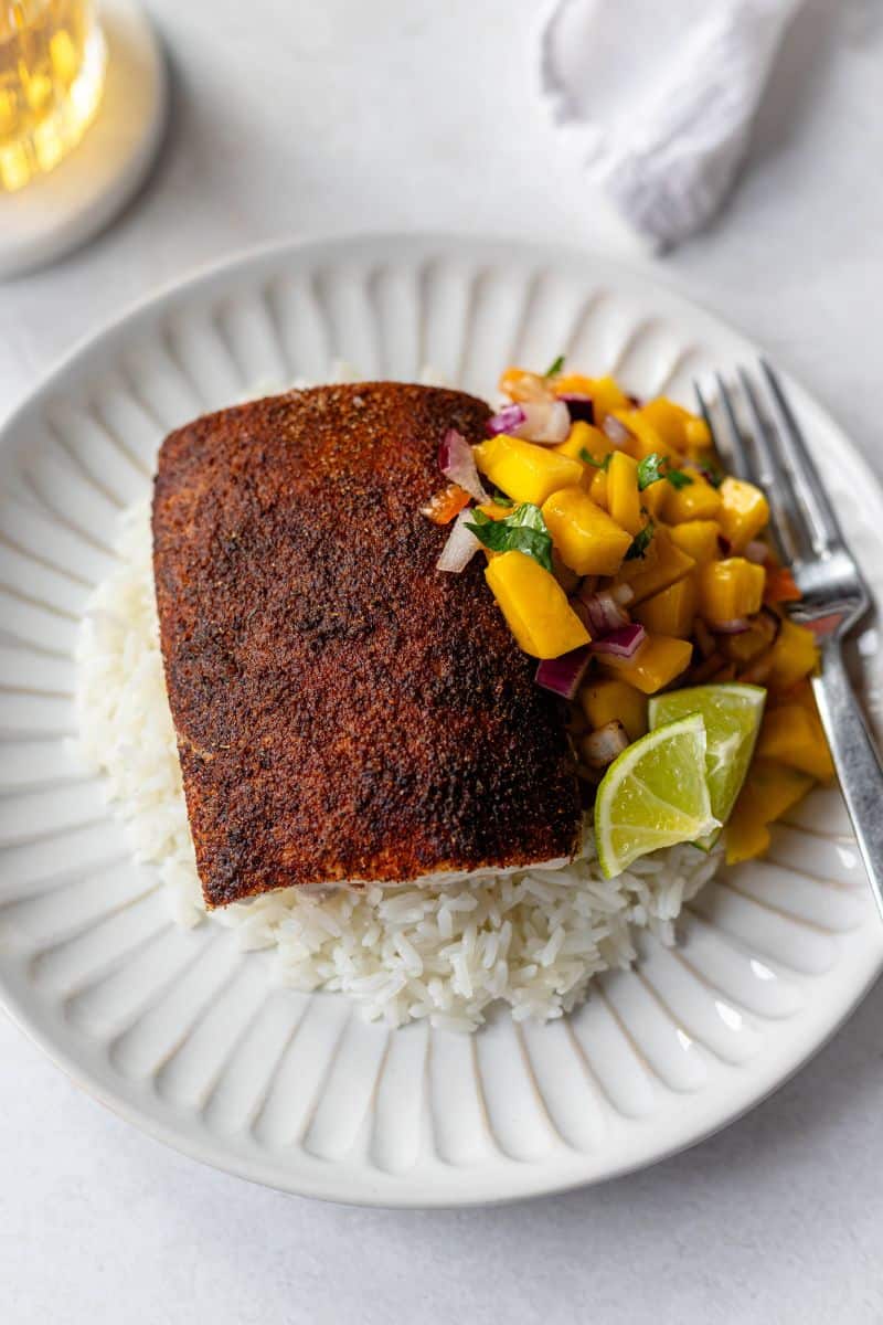 blackened mahi mahi on a bed of white rice served with mango salsa on a white plate.