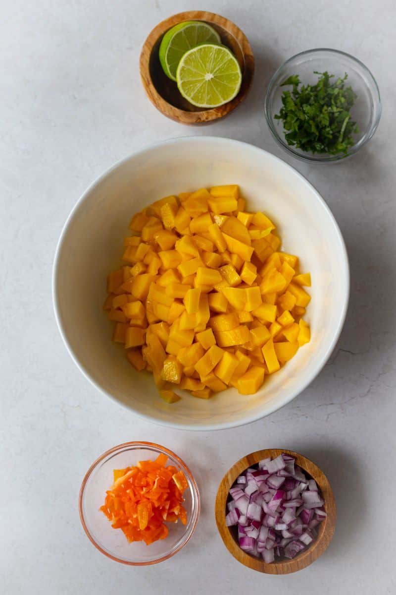 chopped ingredients for mango habanero salsa - lime, cilantro, fresh mango, habanero peppers, red onions.
