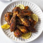 lemon pepper wings garnished with lemon slices and parsley on a white plate.