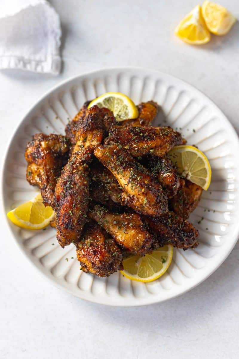 lemon pepper wings tossed in honey on a white plate, garnished with lemon slices and fresh parsley.