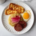 Classic Dominican breakfast (mangu con los tres golpes) on a white plate, served with a cup of black coffee.