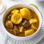 Dominican style sancocho in a white bowl garnished with avocado.