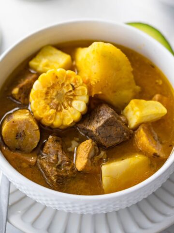 Dominican style sancocho in a white bowl garnished with avocado.