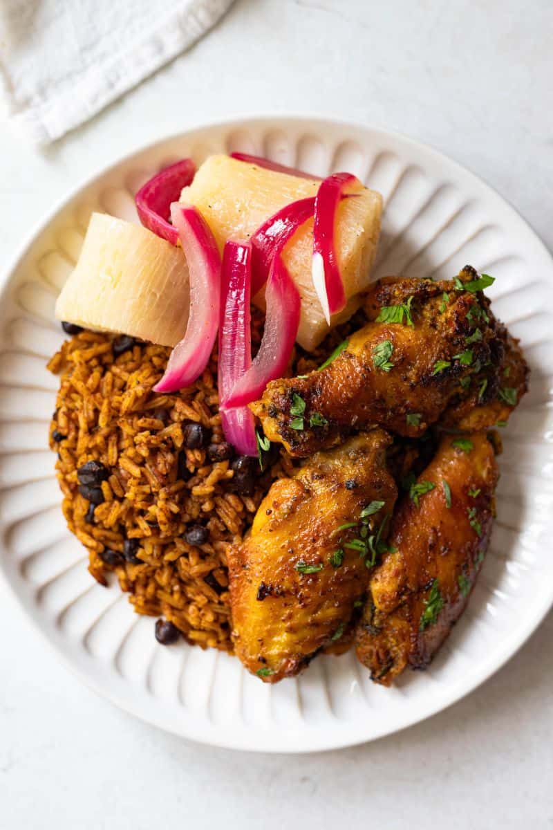 Domincan moro (rice and black beans) on a scalloped plate with chicken wings and yuca with onions.