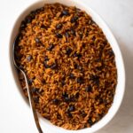 dominican moro (rice and black beans) in a white oval dish with a serving spoon.