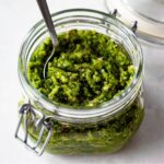 close up of a glass jar of sofrito open with a spoon in it.