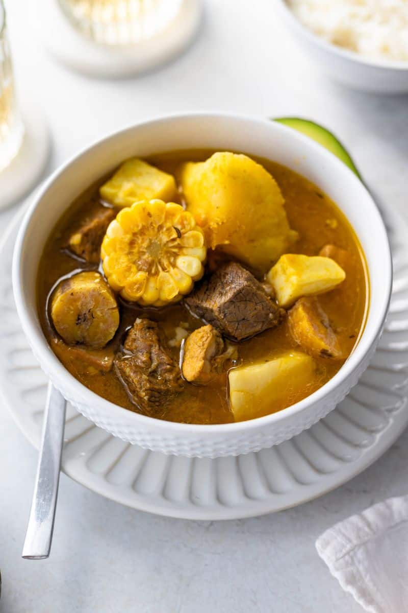 Dominican style sancocho in a white bowl garnished with avocado.