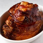 holiday glazed ham with marmalade in a white oval baking dish.