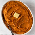 Creamy whipped sweet potatoes topped with butter and thyme in a white oval dish.