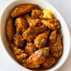 chicken wings tossed in Mozambique sauce in round serving dish.