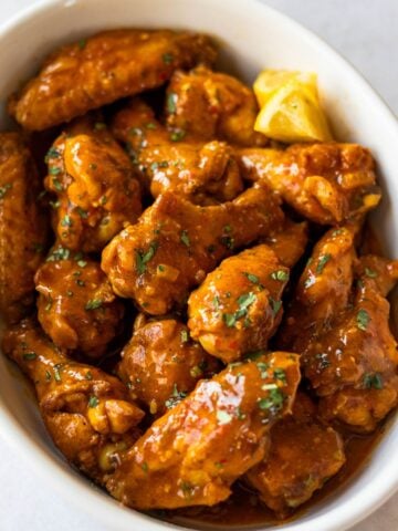 chicken wings tossed in Mozambique sauce in round serving dish.