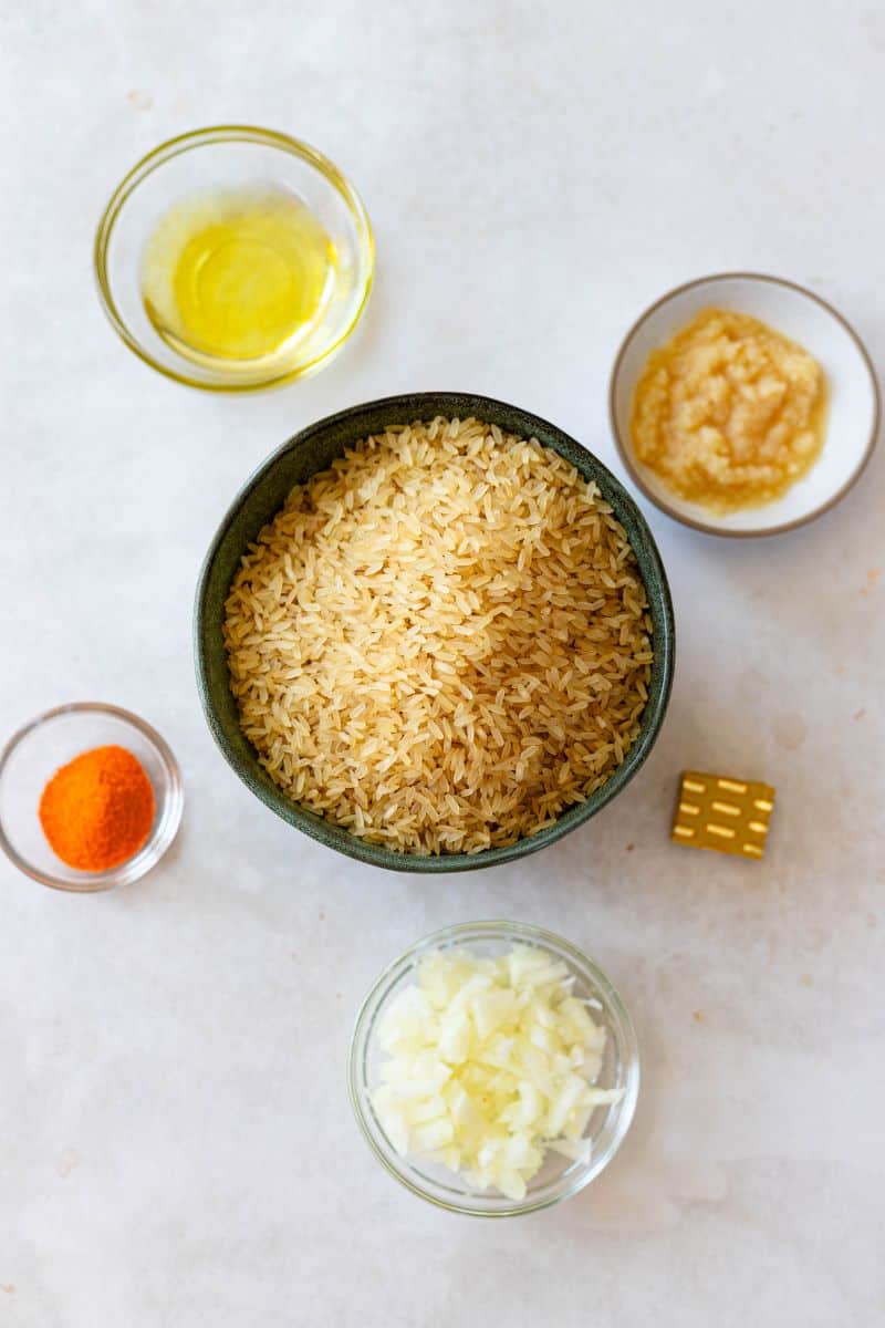 spanish yellow rice ingredients. clockwise from top: olive oil, extra long grain white rice, garlic paste, bouillon cube, onion, sazon with saffron.