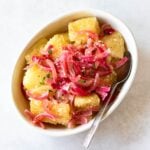 yuca with garlic sauce and red onions in a white serving dish.