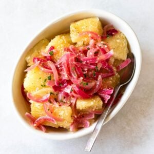 yuca with garlic sauce and red onions in a white serving dish.