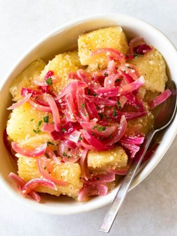 yuca with garlic sauce and red onions in a white serving dish.