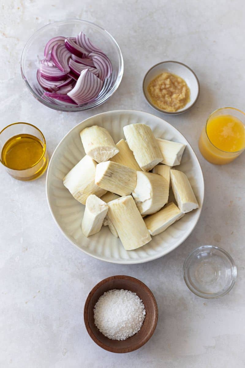 yuca al mojo ingredients: yuca peeled and cut into 2-inch pieces, olive oil, sour orange juice, minced garlic, sliced red onions vinegar and salt are shown.