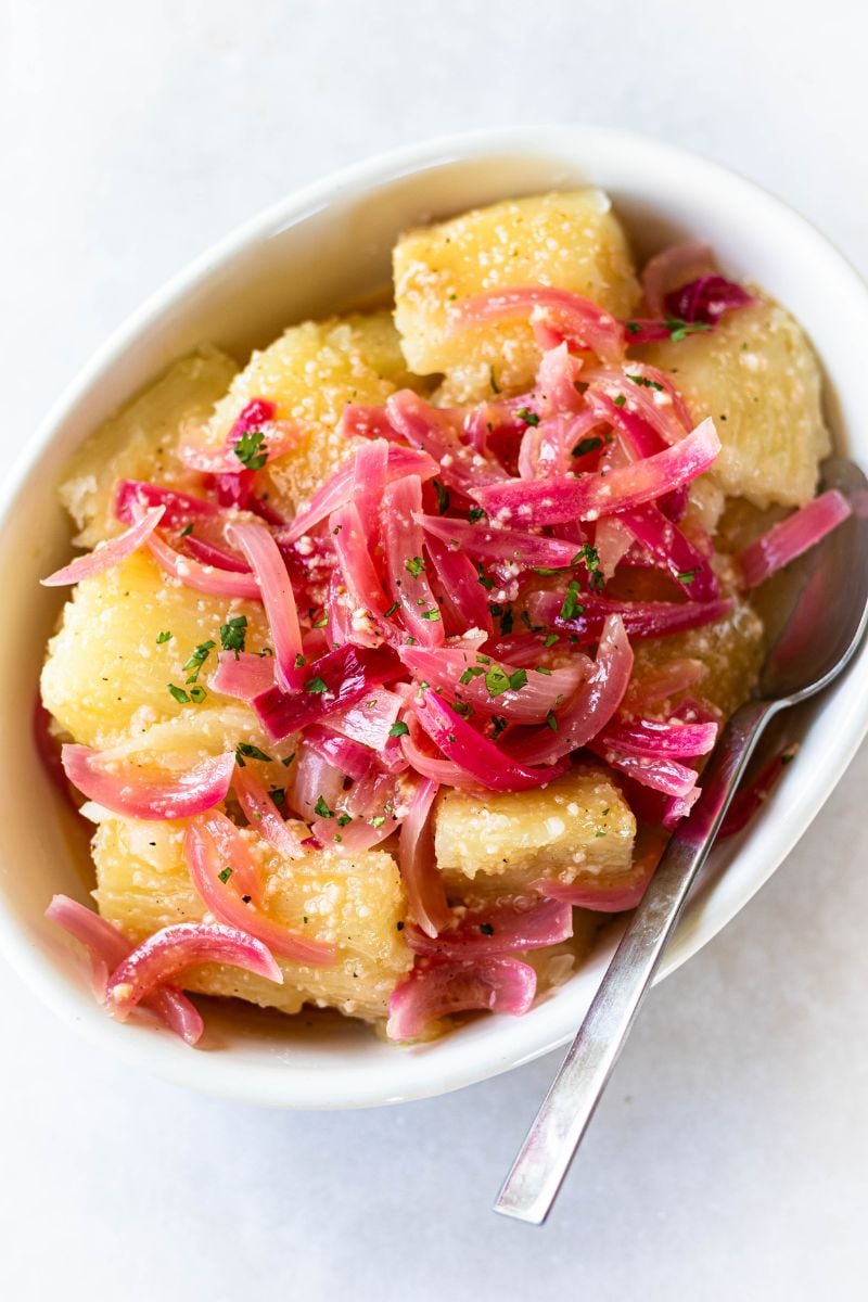 Boiled yuca tossed in garlic citrus mojo with onions in a white bowl.