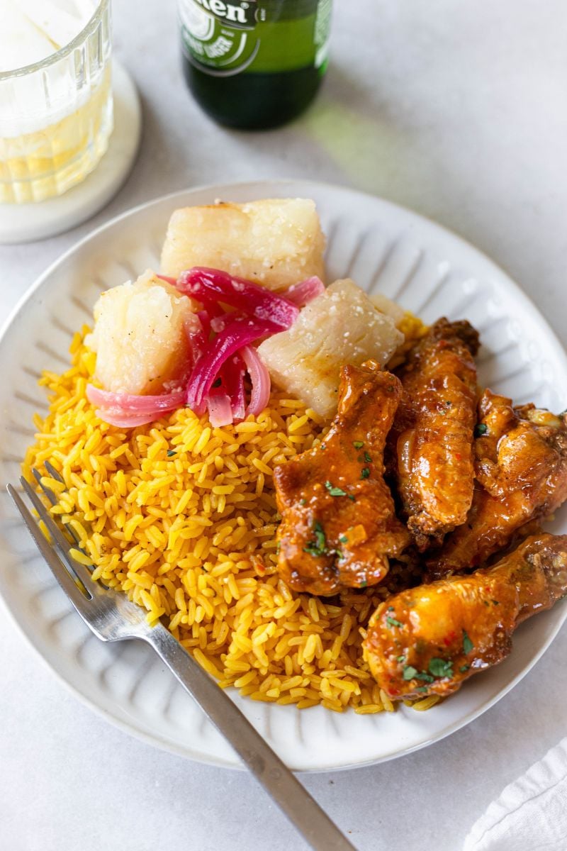 Yuca al mojo, mozambique chicken wings, and yellow rice on a white plate.